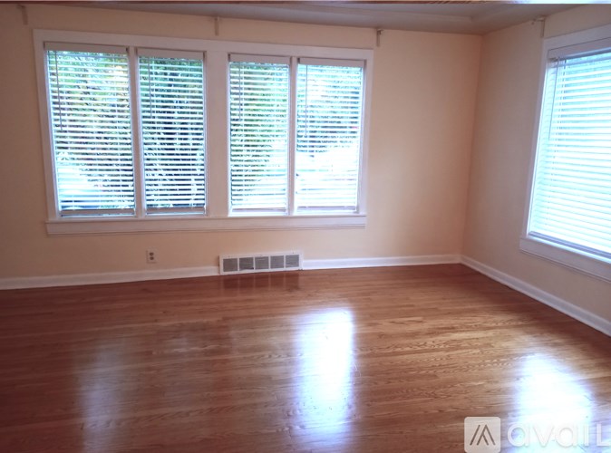 A room with wooden floors and two windows with blinds.
