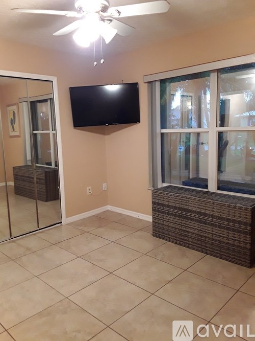 A room with a ceiling fan and a flat screen TV mounted on the wall.