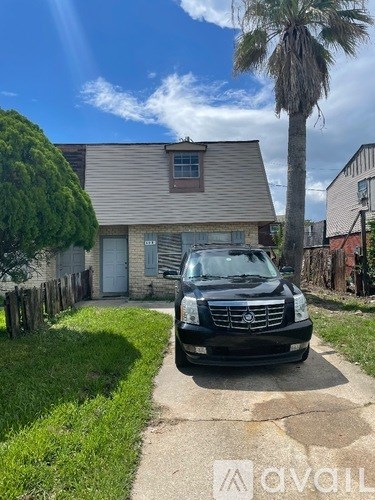 A black SUV is parked in front of a house with a palm tree in the yard.