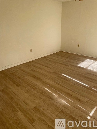 A room with wooden flooring and a window letting in sunlight.