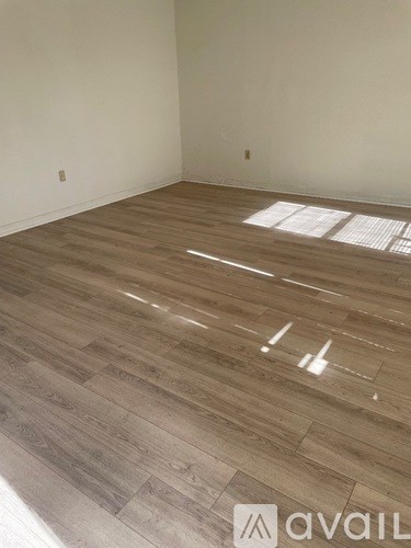 A room with wooden flooring and a window letting in sunlight.