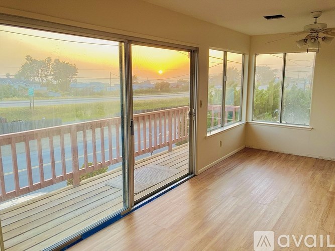 A sunset view from a balcony with a wooden floor and sliding glass doors.