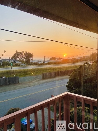 A sunset view from a balcony with a road and houses in the distance.