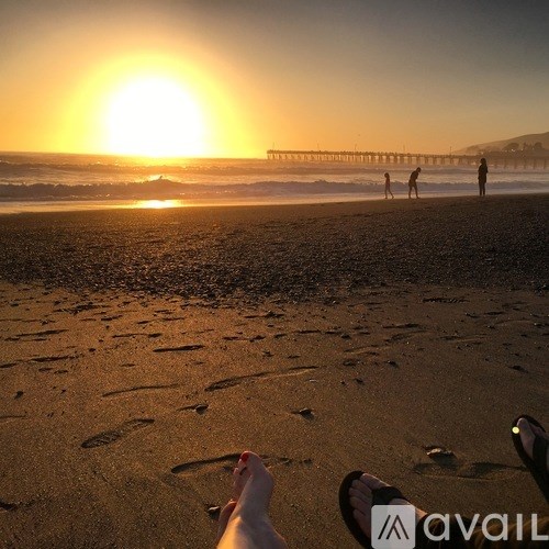 A person is lying down on the beach with their feet in the sand, with the sun setting in the background.