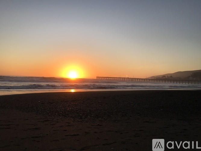 The sun is setting over the ocean with a pier in the distance.
