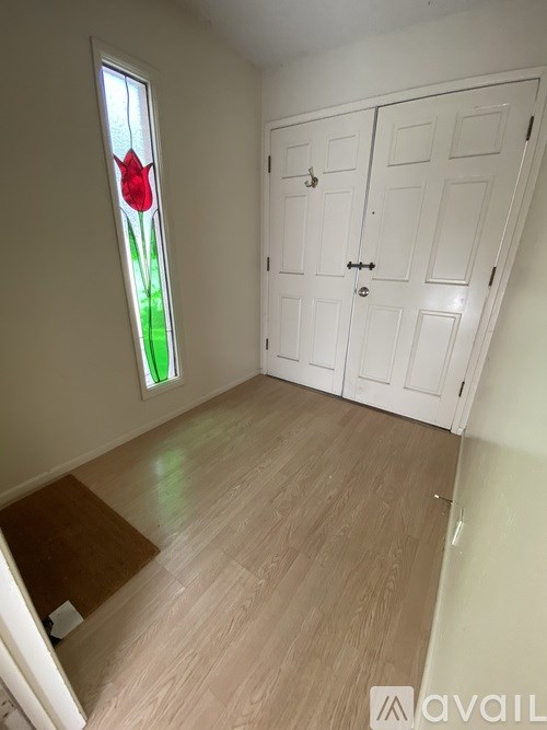 A room with a white wardrobe and a window with a red tulip stained glass.