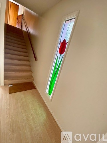 A staircase with a wooden handrail and a stained glass window with a red tulip on it.