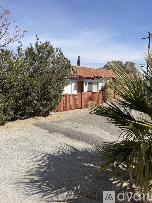A house with a red roof and a brown fence is surrounded by greenery.