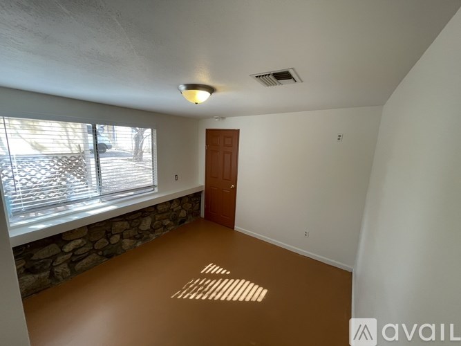 A room with a brown floor and a window with blinds.