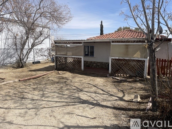 A house with a red tile roof is surrounded by a fence and has a tree in front of it.