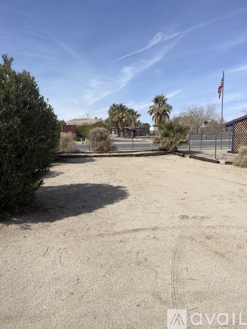 A sandy area with tire tracks leading to a fenced area with a flag.