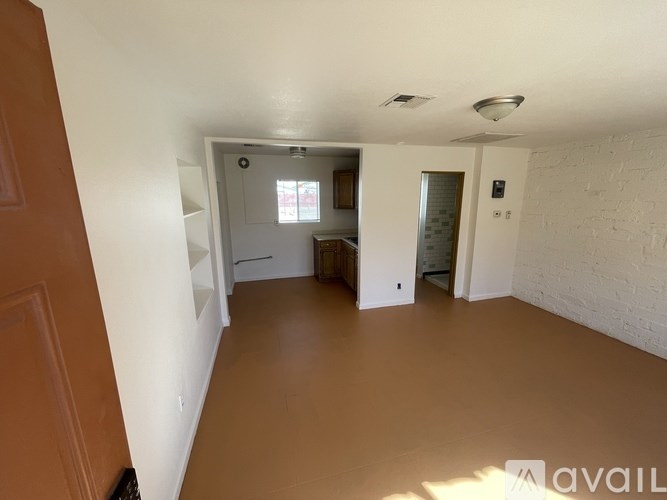 A room with white walls and brown flooring, with a door on the left and a window on the right.