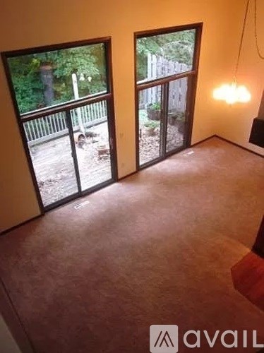 A room with brown carpet and a window overlooking a backyard.