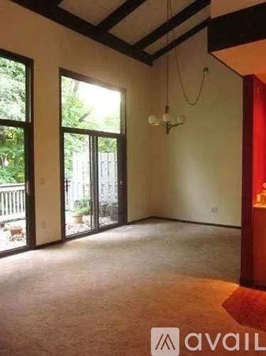 A room with a carpeted floor, a ceiling with wooden beams, and a chandelier hanging from the ceiling.