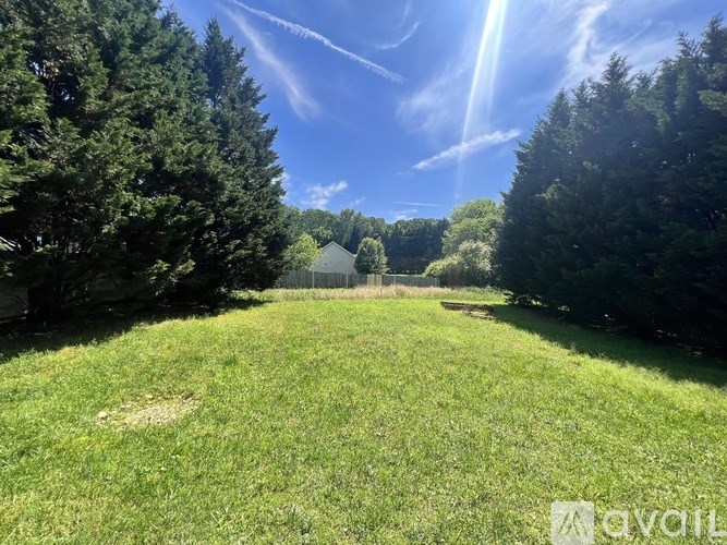 A sunny day in a green field with trees and a house in the distance.