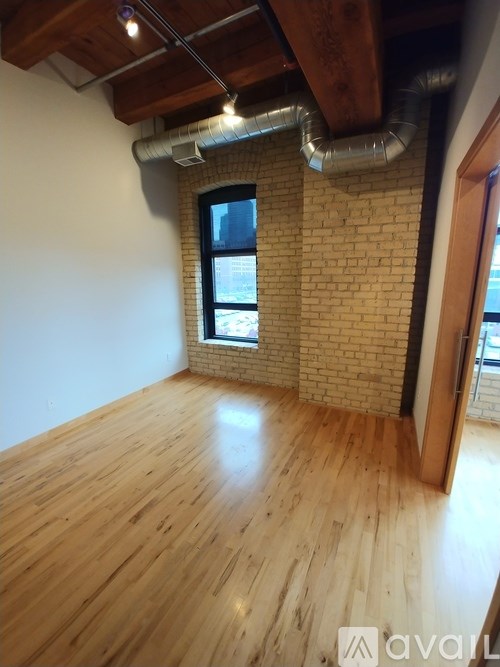 A room with wooden flooring and a brick wall with a window.