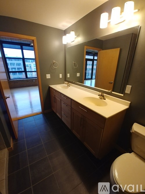 A bathroom with a toilet, sink, mirror and a window.