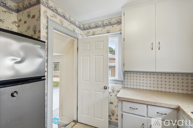 A kitchen with a fridge, cupboards and a doorway leading to a hallway.