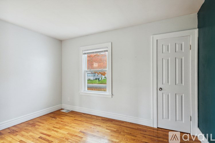 A room with a white door and a window with a view of a street and houses.
