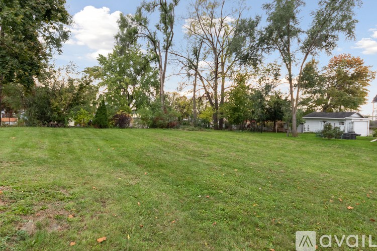 A grassy field with trees and a house in the background.