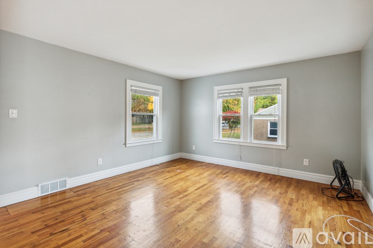 A room with wooden floors and two windows showing a view of a house and trees.