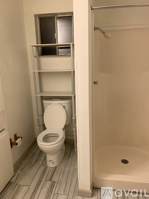 A white toilet with a white toilet paper holder and a white shower stall with a glass door.