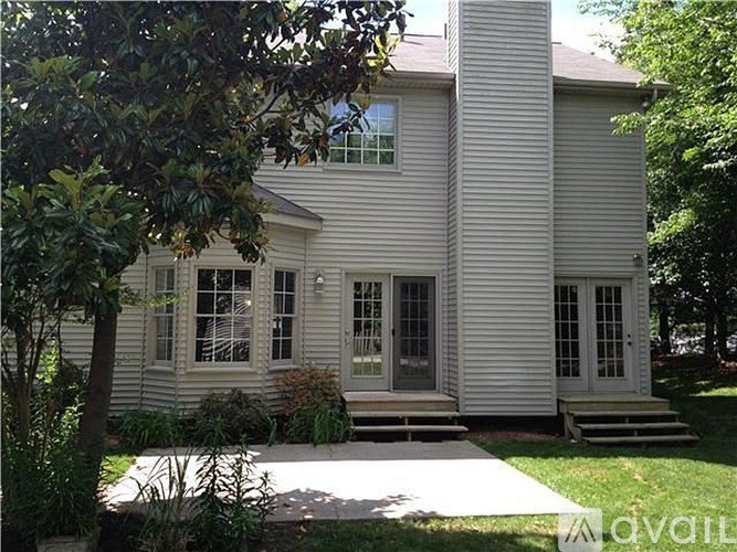 A house with a grey siding and a white door is surrounded by greenery.