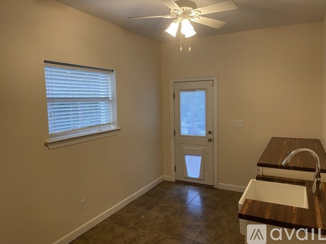 A room with a ceiling fan, a window with blinds, a door, and a kitchenette with a sink and countertop.