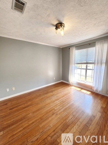 A room with wooden flooring and a window with white curtains.
