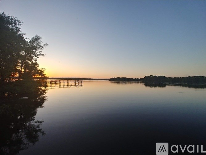 A serene lake with a sunset in the background and a dock extending into the water.