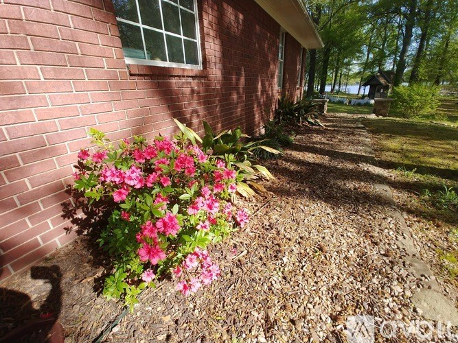A red brick house with a window and a flower bed in front.