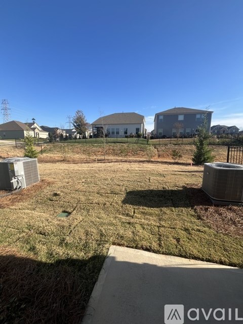 A grassy field with a few houses and trees in the background.