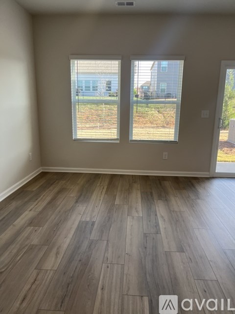 A room with wooden flooring and two windows.