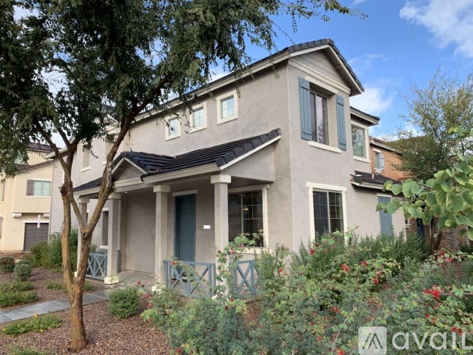 A beige house with a black roof and a tree in front.