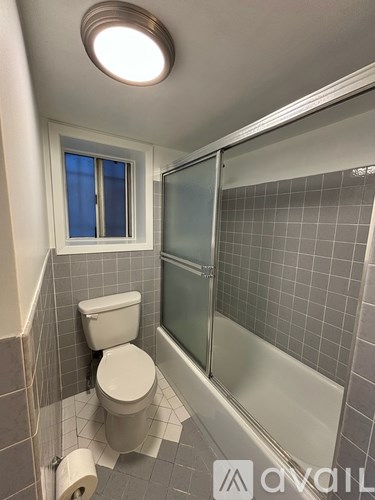 A bathroom with a toilet, a glass shower door, and a window.