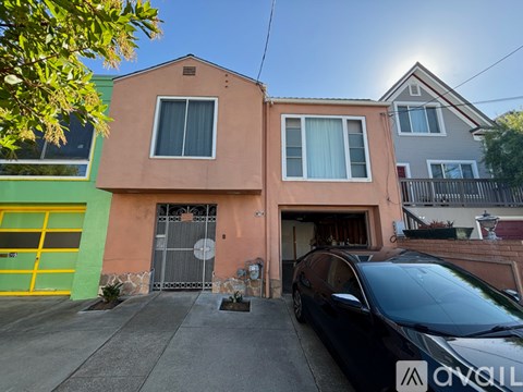 A black car is parked in front of a two-story house with a yellow garage door.