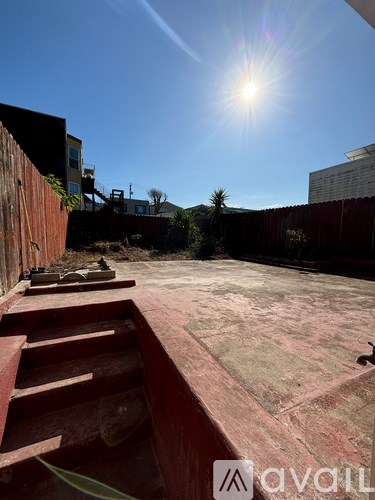 A sunny day in a backyard with a red staircase and a concrete patio.