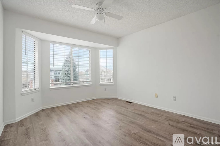 A room with a ceiling fan and a large window overlooking a tree.
