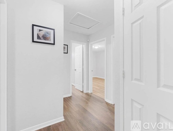 A hallway with white walls and wooden floors leading to a door.
