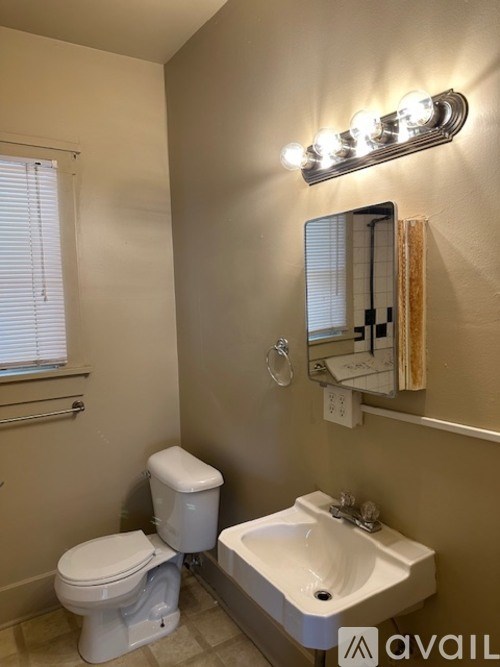 A bathroom with a toilet, sink, mirror, and light fixture.