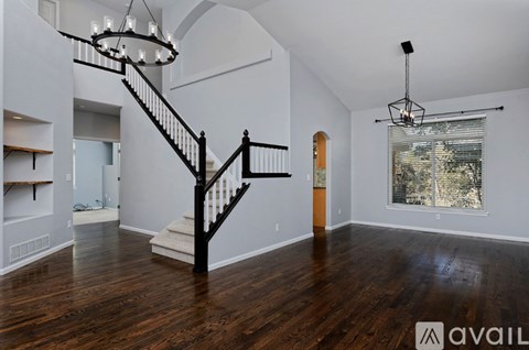 A spacious room with a wooden floor and a staircase with a black railing.