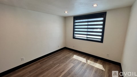 A room with wooden flooring and a window with blinds.