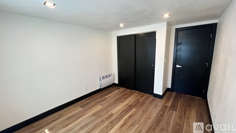 A room with wooden flooring and two black doors.