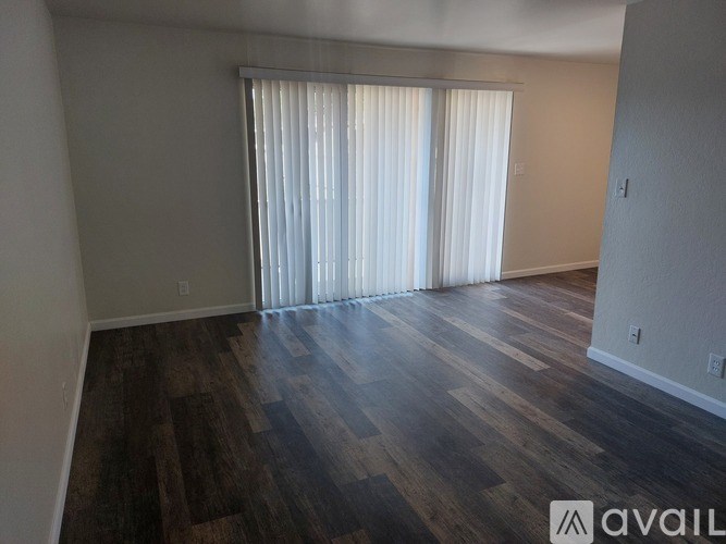 A room with wooden flooring and a window with white curtains.