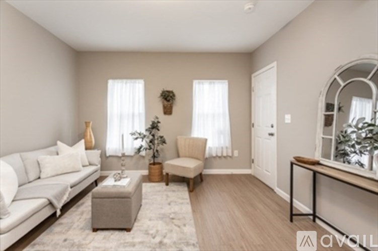 A living room with a white sofa, a grey ottoman, a wooden coffee table, and a mirror on the wall.