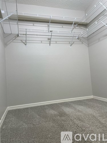 A room with a grey carpet and white walls with a metal shelf above it.