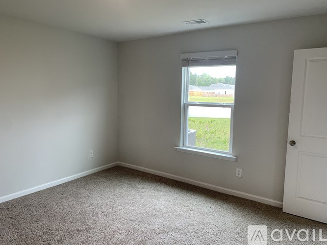 A room with a carpeted floor and a window overlooking a field.