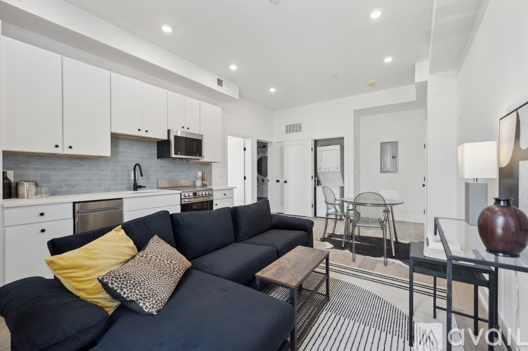 A modern living room with a black sofa and a kitchen area in the background.