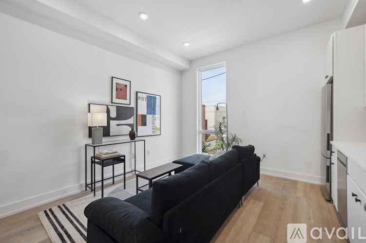A living room with a black couch and a small table with a lamp on it.