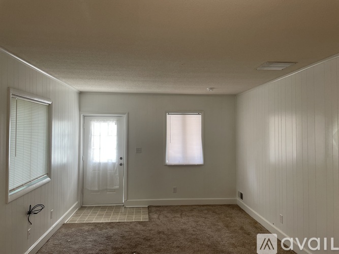 A room with a carpeted floor, a door, and a window with blinds.